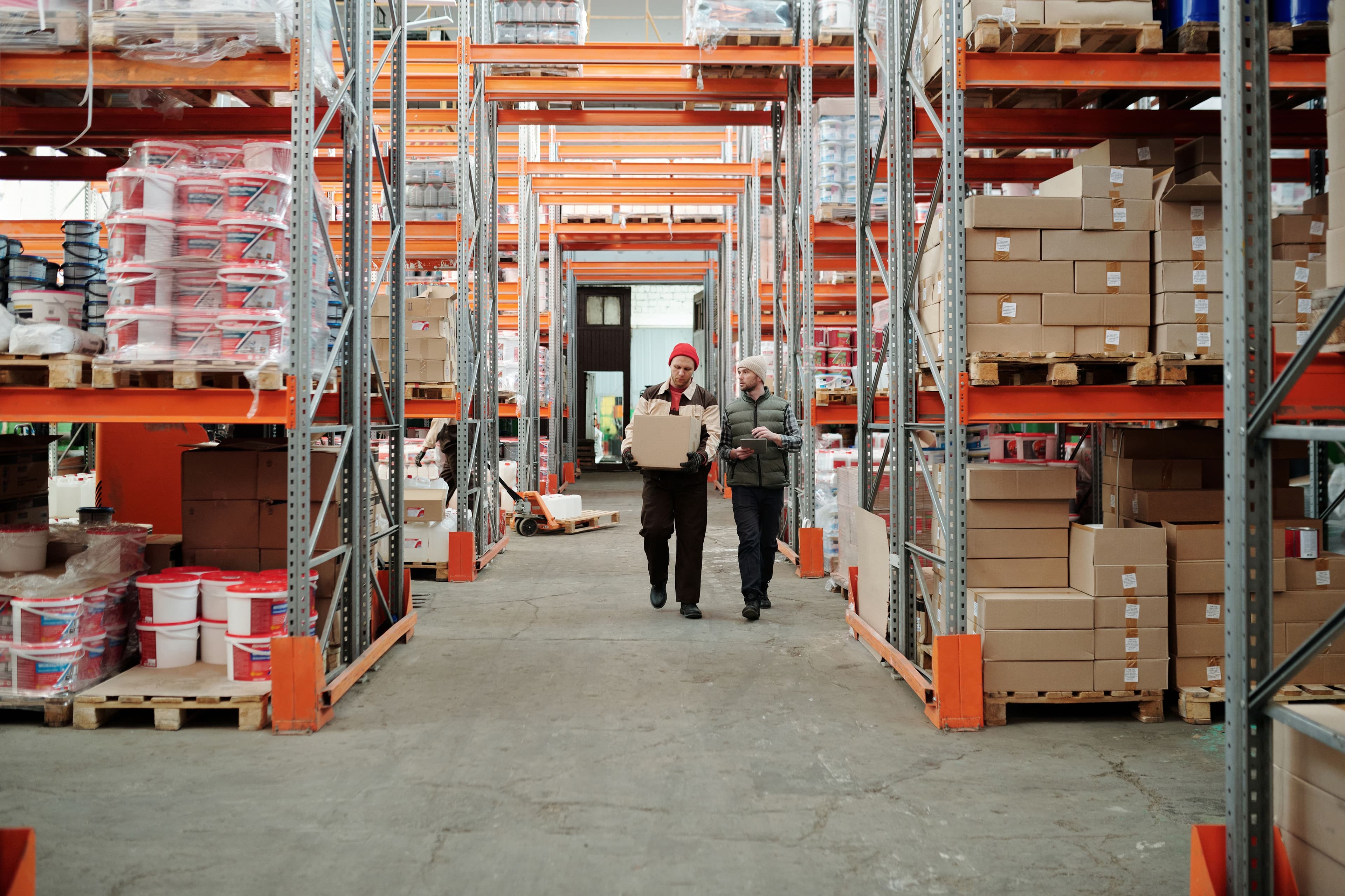 Warehouse workers moving boxes with a pallet truck on the floor of a distribution center.