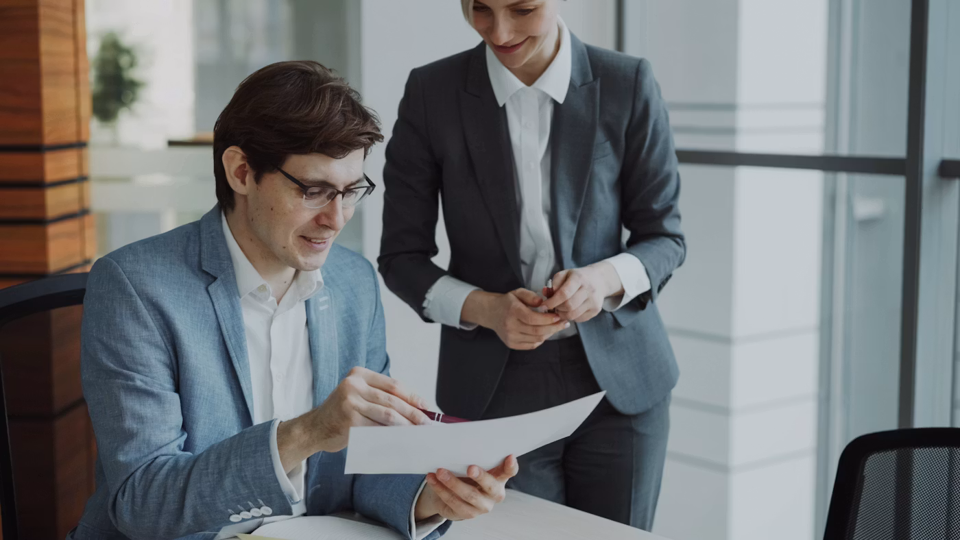 Two colleagues at a desk reviewing paperwork together.